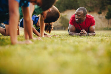 Happy school coach training a rugby team in a field. Male instructor having a practice session with his students in a school. Sports mentorship in primary school. - JLPSF28915