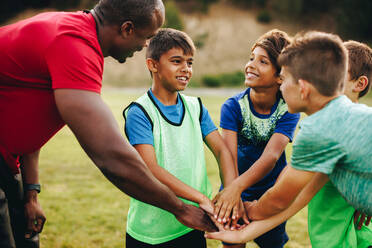 Sports trainer having a huddle with his team in a school field. Rugby coach giving his students a motivational talk before practice. Sports mentorship in elementary school. - JLPSF28919