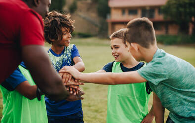 Schulkinder, die mit ihrem Trainer auf einem Sportplatz zusammensitzen. Rugby-Team, das vor dem Training eine motivierende Ansprache hält. Sportlehrer, der Kinder in der Grundschule betreut. - JLPSF28920