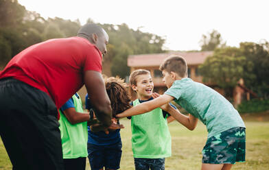 Schulsportteam bei einer Besprechung auf einem Rugbyfeld. Trainer, der seine Schüler vor dem Training motiviert. Sportlehrer, der Kinder in der Grundschule betreut. - JLPSF28921