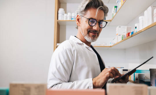 Älterer Apotheker bei der Inventur mit einer Tablette in einer Drogerie. Älterer Mann beim Zählen des medizinischen Inventars anhand einer Checkliste in einer Apotheke. - JLPSF28927