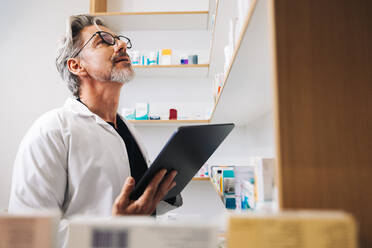 Pharmacist looking for prescription medication on a drug store shelf. Senior man using a digital tablet to fill online prescriptions in a pharmacy. - JLPSF28928