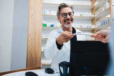 Pharmacist receiving a prescription from a patient in a drug store. Happy healthcare provider filling a doctor's prescription in a pharmacy. - JLPSF28940