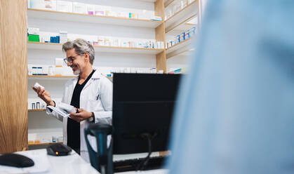 Älterer Apotheker, der das Etikett eines Medikaments liest, während er einem Patienten in einer Apotheke hilft. Medizinisches Fachpersonal, das ein ärztliches Rezept in einer Apotheke ausstellt. - JLPSF28943