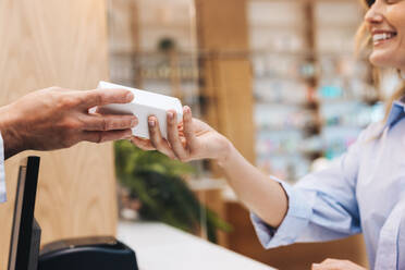 Pharmacist handing a patient a box of pills in a drug store. Healthcare worker dispensing medication over the counter in a pharmacy. - JLPSF28946