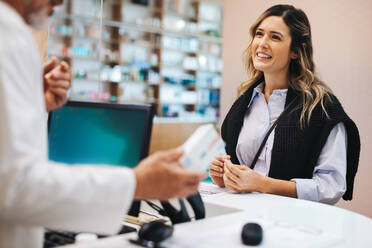 Female patient talking to a pharmacist over the counter. Healthcare provider assisting a woman with medication in a drug store. - JLPSF28949