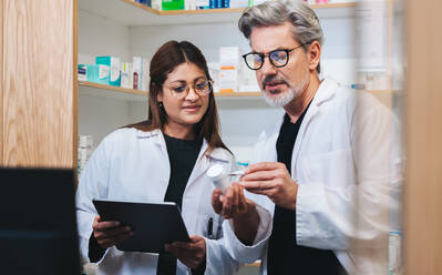 Healthcare providers filling online prescriptions in a pharmacy. Two mature pharmacists reading a medication label. Man and woman working together in a drug store. - JLPSF28953