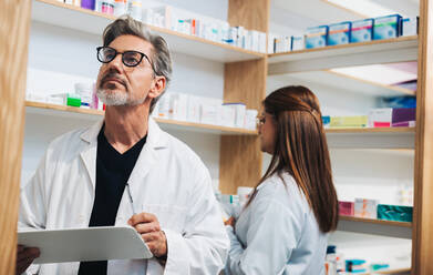 Pharmacist doing an inventory take while working in a drug store with his colleague. Senior healthcare worker counting stock in a pharmacy. - JLPSF28957