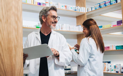 Ein leitender Apotheker arbeitet mit einem Kollegen in einer Apotheke. Zwei erfahrene Mitarbeiter des Gesundheitswesens führen eine Inventur in einer Apotheke durch. - JLPSF28958