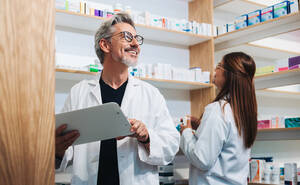 Älterer Apotheker bei der Arbeit mit einem Kollegen in einer Apotheke. Zwei glückliche Fachkräfte des Gesundheitswesens bei einer Bestandsaufnahme in einer Drogerie. - JLPSF28959