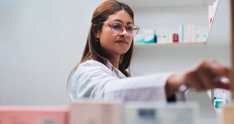 Female drug store worker getting medication from a shelf. Pharmacist filling a prescription in a chemist. Female healthcare worker in a pharmacy. - JLPSF28961