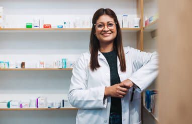 Female pharmacist standing in a drug store and looking at the camera. Happy woman working in a pharmacy. Portrait of a female healthcare worker in a chemist. - JLPSF28963