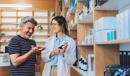 Pharmacist recommending a skincare product to a patient in a chemist. Female healthcare professional assisting a man in a pharmacy. - JLPSF28978