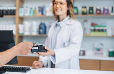 Pharmacist scanning a credit card on a card machine in a drug store. Female healthcare worker receiving payment for medication in a pharmacy. - JLPSF28979