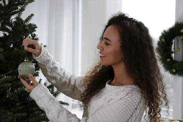 Lächelnde Frau beim Schmücken des Weihnachtsbaums mit Kugeln zu Hause - SYEF00151