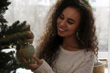 Glückliche Frau schmückt Weihnachtsbaum mit Christbaumkugel zu Hause - SYEF00152