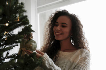 Glückliche junge Frau beim Schmücken des Weihnachtsbaums mit Kugeln zu Hause - SYEF00154