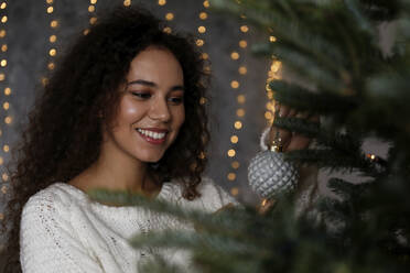 Schöne junge Frau beim Schmücken des Weihnachtsbaums zu Hause - SYEF00163