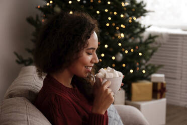 Glückliche Frau mit einer Tasse Marshmallow-Kakao auf dem Sofa zu Hause - SYEF00173