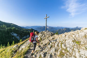 Deutschland, Bayern, Wanderin beim Vorbeigehen am Gipfelkreuz auf dem Taubenstein - FOF13257