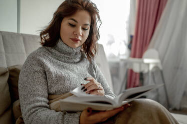 Beautiful young woman reading book at home - ANAF00749