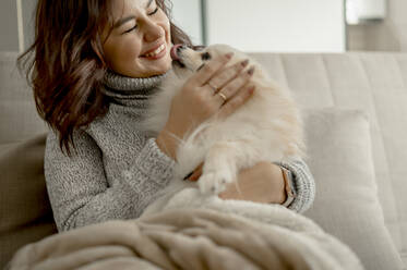 Happy young woman stroking Pomeranian dog at home - ANAF00751