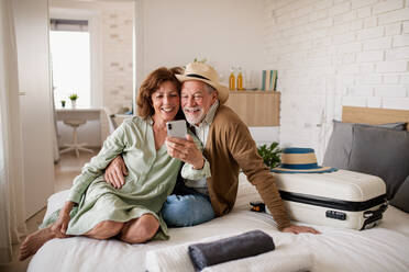 Porträt eines glücklichen älteren Paares mit Smartphone im Hotelzimmer, das ein Selfie macht. - HPIF05332