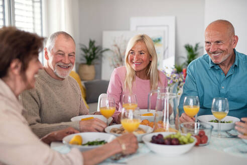 Eine Gruppe älterer Freunde feiert drinnen eine Party und unterhält sich beim Essen am Tisch. - HPIF05342