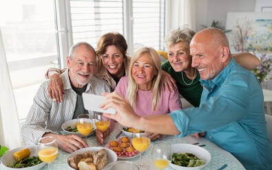 A group of senior friends having party indoors, taking selfie when eating at the table. - HPIF05344