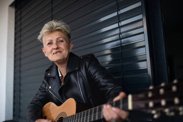 A portrait of senior woman with cigarette standing against black backround, playing guitar. - HPIF05364