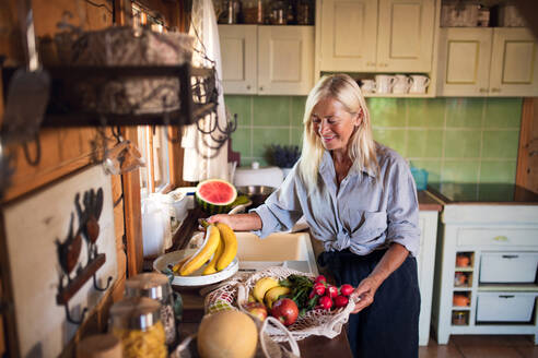 A happy senior woman unpacking shopping indoors at home, sustainable lifestyle. - HPIF05367