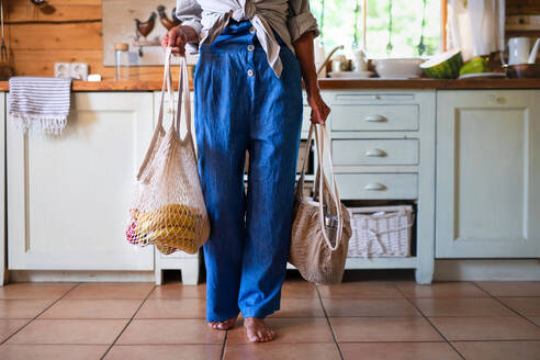 A waist down of senior woman holding reusable shopping bags indoors at home sustainable lifestyle. - HPIF05373