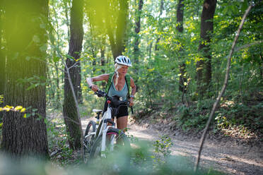 An active senior woman biker pushing ebike outdoors in forest. - HPIF05389