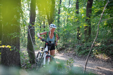 Eine aktive ältere Radfahrerin, die ihr E-Bike im Wald schiebt. - HPIF05389