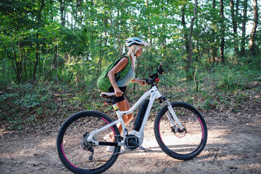 An active senior woman biker pushing ebike outdoors in forest. - HPIF05390