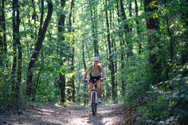 A front view of active senior woman biker cycling outdoors in forest. - HPIF05393