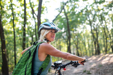 An active senior woman biker pushing bike outdoors in forest. - HPIF05394