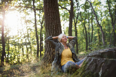 A portrait of senior woman relaxing and sitting with eyes closed outdoors in forest. - HPIF05404