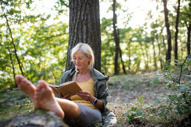 Eine ältere Frau entspannt sich und liest ein Buch im Freien im Wald. - HPIF05407