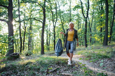 Eine ältere Umweltschützerin mit Müllsack beim Aufsammeln von Abfällen im Freien im Wald. - HPIF05412