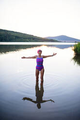 Ein Porträt einer aktiven älteren Schwimmerin, die sich im Freien in einem See ausstreckt. - HPIF05418