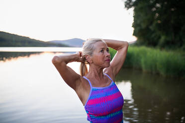 Ein Porträt einer aktiven älteren Schwimmerin, die sich im Freien in einem See ausstreckt. - HPIF05419