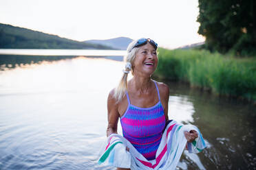 Ein Porträt einer aktiven älteren Schwimmerin, die sich mit einem Handtuch im Freien am See abtrocknet. - HPIF05421