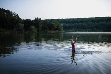 Ein Porträt einer aktiven älteren Schwimmerin, die sich im Freien in einem See ausstreckt. - HPIF05425