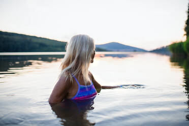 A side view of active senior woman swimmer diving outdoors in lake. - HPIF05426