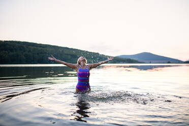 A portrait of active senior woman swimmer standing and stretching outdoors in lake. - HPIF05430