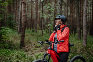 Eine ältere Frau Radfahrer setzen auf Fahrradhelm im Freien im Wald im Herbst Tag. - HPIF05437