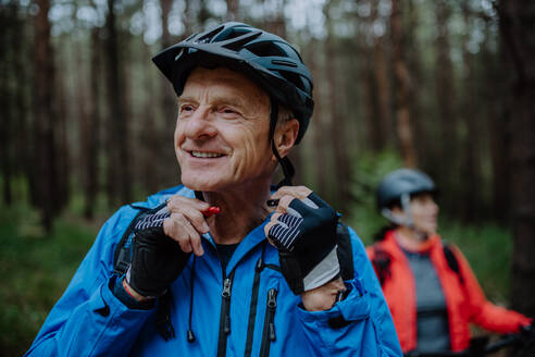 Ein älteres Paar Radfahrer setzen auf Fahrradhelm im Freien im Wald im Herbst Tag. - HPIF05438