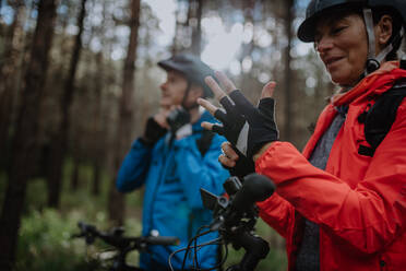 Ein älteres Paar Radfahrer setzen auf Fahrradhelm und Handschuhe im Freien im Wald im Herbst Tag. - HPIF05440