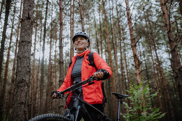 Ein niedriger Winkel Blick auf ältere Frau Biker zu Fuß und schieben Fahrrad im Freien im Wald im Herbst Tag. - HPIF05441